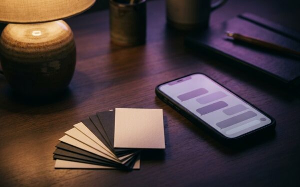 A dark desk lit by one lamp: a phone showing abstract chat bubbles beside a fan of cards, most face down.